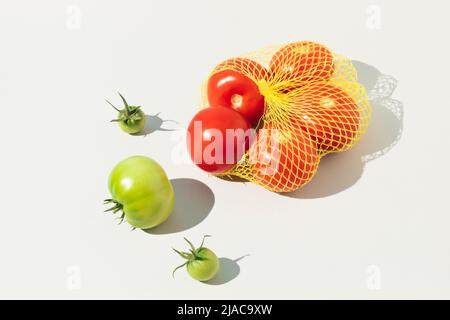 Green unripe tomato and red ripe tomatoes in bag isolated on white background. Minimal food concept. Stock Photo