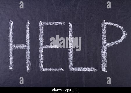 Handwritten chalk inscription HELP on black chalkboard close up. Help word written on blackboard. Stock Photo