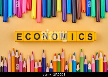 The word ECONOMICS written on plastic cubes in frame from colored school supplies. Flat lay. Stock Photo
