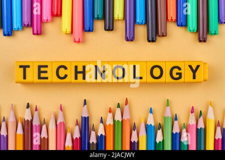 The word technology written on yellow cubes. Flat lay with colorful pencils. Devices concept. Stock Photo