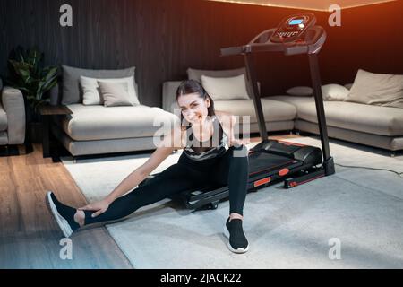 cheerful female stretching and preparing for cardio workout on treadmill at home Stock Photo