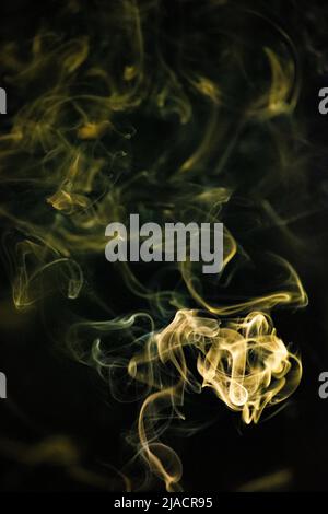 A Golden yellow swirling, ascending smoke pattern with a black background, photo could be used as a background, smoke texture or abstract, or general Stock Photo