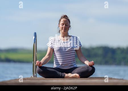 Woman sitting cross-legged on a dock meditating, Wallersee, Salzburg, Austria Stock Photo