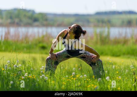 Woman doing standing cat cow yoga pose by Wallersee, Salzburg, Austria Stock Photo