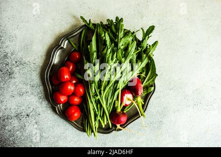 Overhead view of fresh rocket, cherry tomatoes and radishes on a pewter plate Stock Photo