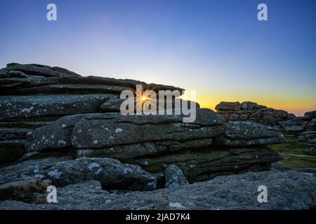 Sunburst through a granite tor, Dartmoor National Park, Devon, England, UK Stock Photo