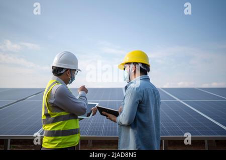 Two engineers standing next to solar panels at a solar powered station talking, Thailand Stock Photo