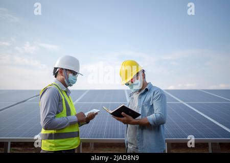 Two engineers standing next to solar panels at a solar powered station looking at a notebook and digital tablet, Thailand Stock Photo