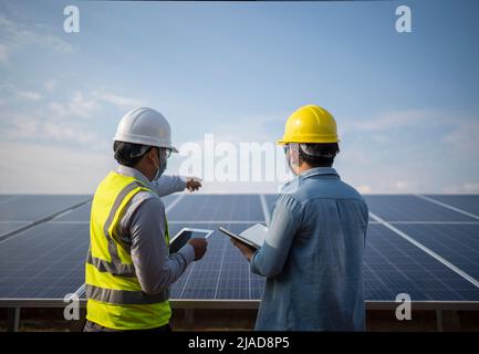 Two engineers standing next to solar panels at a solar powered station talking, Thailand Stock Photo