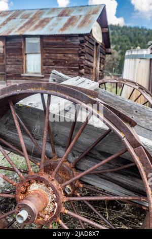 Molson, WA - USA: 05-10-2022: Old wood wagon, close-up of wheel with log cabin in background Stock Photo