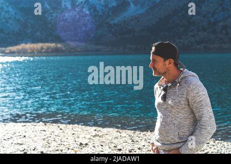 Man standing in front of mountain lake with ball cap on looking away  Stock Photo