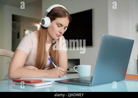 Woman teenager in headphone using laptop for online study from home office Stock Photo