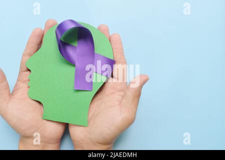 Hand holding human head profile with purple awareness ribbon on brain. Alzheimer's Disease, ADHD, ADD, Epilepsy, Cystic Fibrosis, Thyroid Pancreatic. Stock Photo