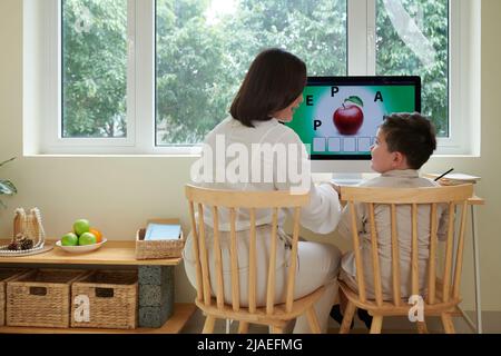 Home tutor teaching boy English language while they are sitting at computer desk Stock Photo