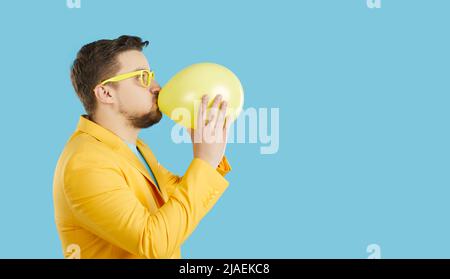 Young man blow air balloon on blue background Stock Photo