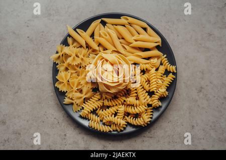 Different Types of Pasta Laid Up on the Black Plate on the Table Stock Photo
