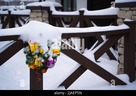 Winter view - snow covered christmas wreath hanging on wooden porch railing with stone pillars Stock Photo