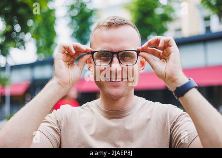 Happy african casual man in glasses sits at cafe table looking at camera, cheerful black student posing studying with book in coffee house, smiling bu Stock Photo