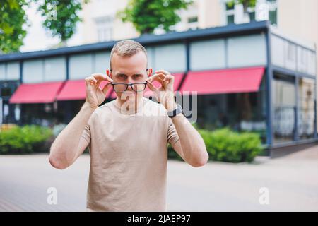 Happy african casual man in glasses sits at cafe table looking at camera, cheerful black student posing studying with book in coffee house, smiling bu Stock Photo