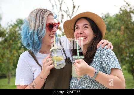 Two female happy friends drinking refreshing drinks, laughing and hugging. Stock Photo