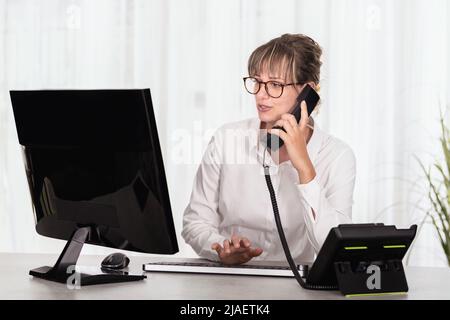 Front view of a businesswoman with eyeglass using computer and talking on the phone Stock Photo