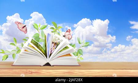 Book of nature. Horizontal banner with book open, green leaves and two butterflies on wood table. Knowledge, education, ecology and environment concep Stock Photo