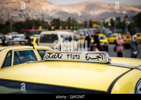 Damascus, Syria - May, 2022: Taxi sign closeup on Taxi car in street traffic of Damascus