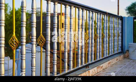 Beautiful decorative cast metal wrought fence with artistic forging. Iron guardrail close up. Golden chromium silver fence closeup. Stock Photo