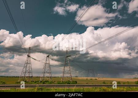 Power lines against the dramatic sky. Countryside field with power line pylons. Stock Photo