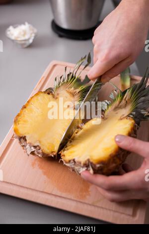 Unrecognizable man cutting a pineapple on chopping board. Stock Photo