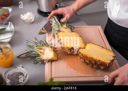 Unrecognizable man cutting a pineapple on chopping board. Stock Photo