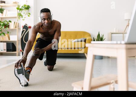 Young adult african man training and stretching while watching fitness video Stock Photo