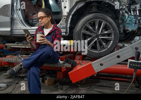 Female auto mechanic using smartphone in car garage Stock Photo