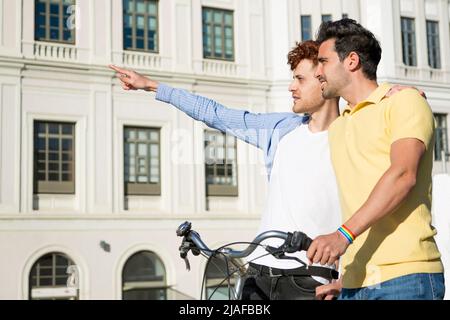 Gay young men couple pointing fingers with rainbow bracelet and bicycle outdoors. lgbt relationship concept Stock Photo