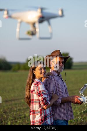 Two farmers senior man and young woman driving drone with remote control in corn field in spring time Stock Photo