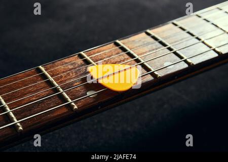 Yellow pick between the strings of an electric guitar close up. Guitar neck with rosewood fingerboard and pick Stock Photo