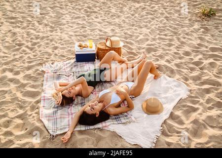 Young two women talking and smiling while lying on beach Stock Photo