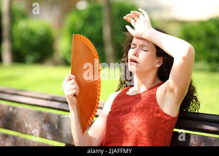 Woman in a park suffering heat stroke fanning Stock Photo