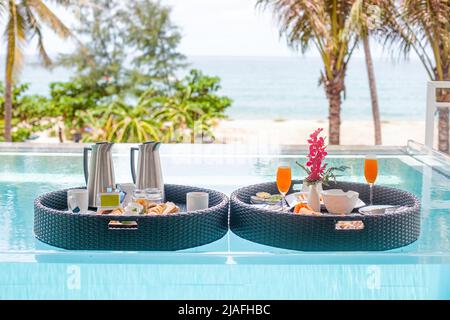 Breakfast in swimming pool, floating breakfast in tropical resort. Healthy breakfast with fruit juice on floating tray in resort pool Stock Photo