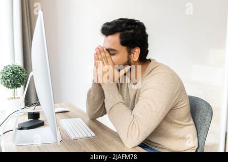 Tired businessman frown while checking financial documents, touching forehead with the arm, sitting in the trendy office at the laptop, consulting client online, analyze statistic, overworked Stock Photo