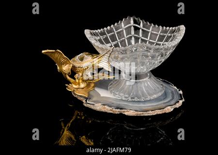 Gilded luxury crystal caviar bowl on stand made of natural quartz, carved brass fish figurine on a black background. Stock Photo