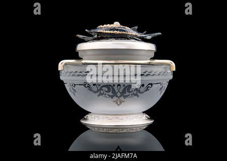 Gilded luxury crystal caviar bowl on stand made of natural quartz, carved brass fish figurine on a black background. Stock Photo