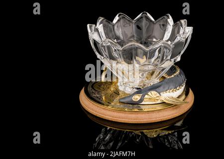 Gilded luxury crystal caviar bowl on stand made of natural quartz, carved brass fish figurine on a black background. Stock Photo