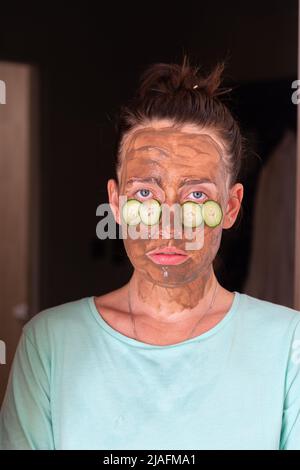 A girl in a cosmetic mask and cucumber slices under her eyes. A young woman takes care of her facial skin by applying cosmetics. Stock Photo