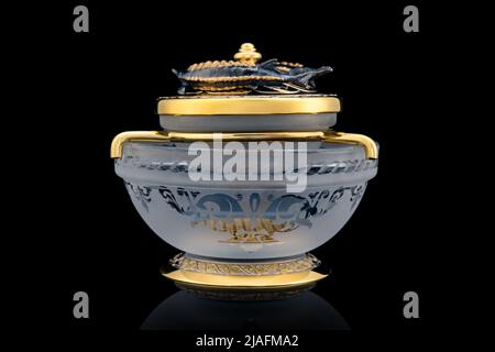 Gilded luxury crystal caviar bowl on stand made of natural quartz, carved brass fish figurine on a black background. Stock Photo