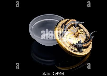 Gilded luxury crystal caviar bowl on stand made of natural quartz, carved brass fish figurine on a black background. Stock Photo