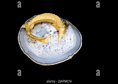 Gilded luxury crystal caviar bowl on stand made of natural quartz, carved brass fish figurine on a black background. Stock Photo