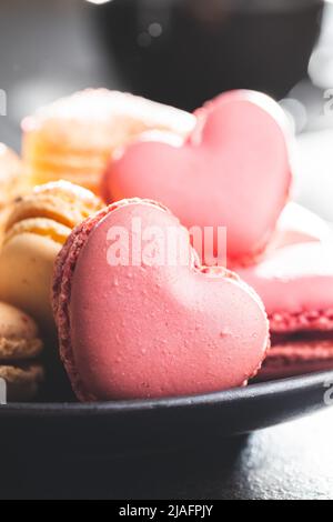 Heart shaped Sweet macarons on plate on a black table. Stock Photo