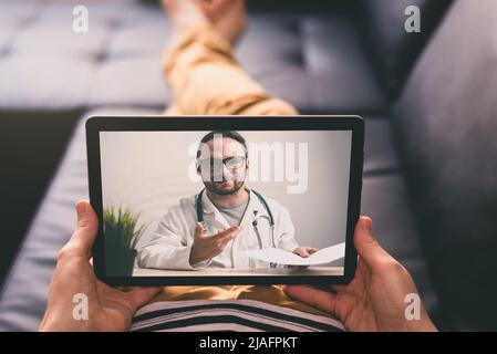 Woman lying on a sofa and talking with a doctor online using digital tablet. Telemedicine concept. Stock Photo