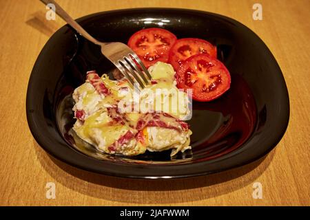 Baked meat with cheese and fresh tomatoes in a black plate on the table Stock Photo